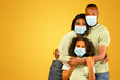 © Prostock-studio - Young african american parents and their daughter wearing protective medical masks, embracing and looking at camera over yellow background. Black family following measures against coronavirus