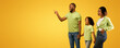 © Prostock-studio - Positive african american family of three looking aside, young man pointing finger at copy space, standing on yellow background, demonstrating empty place for your advertisement, panorama