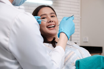 Wall Mural - Asian male dentist examines beautiful young female patient's teeth stomatology in dental clinic, well-being hygiene checks, and professional orthodontic healthcare work in doctor's office hospital.