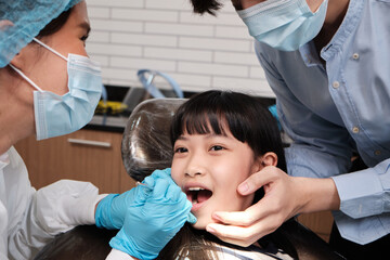 Asian female pediatric dentist examines a girl's teeth in dental clinic and takes care and encourages of father, mouth oral hygiene, and professional orthodontic healthcare work in a kid hospital.