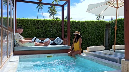 Wall Mural - a couple enjoy a tranquil afternoon by a private pool. The sun shines brightly, enhancing their peaceful escape. Digital Nomad at work or freelancer with laptop in private pool villa