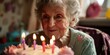 © HO - An elderly person smiling while blowing out candles on a cake, celebrating a milestone birthday.