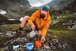 © EVERST - Man setting up backcountry kitchen to prepare dinner cooking camping meals using gas stove outdoor gear on picnic in mountains - travel solo hiking survival trip adventure vacations summer eco tourism