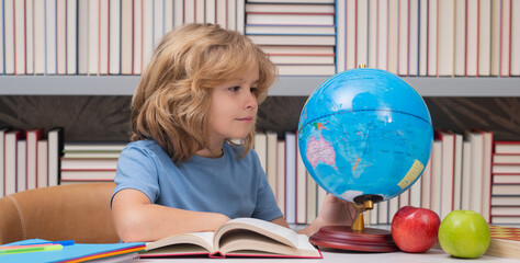 Fototapete - Pupil looking at globe in library at the elementary school. Back to school. Portrait of cute child school boy. Clever kid with school supplies.