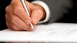 © Jss - A close-up of a hand holding a pen, signing a document on a white sheet of paper, indicating a formal or professional process.