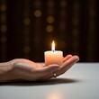 © Shavy - a single burning candle held in a hand against a dark bokeh background