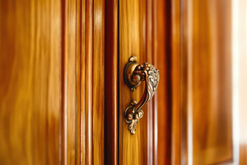 Ornate vintage brass handle on polished wooden cabinet door