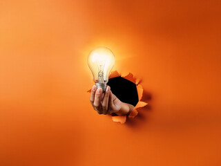 Poster - A hand emerges from a torn orange background, holding a glowing lightbulb.  It symbolizes a breakthrough, a new idea shining through.