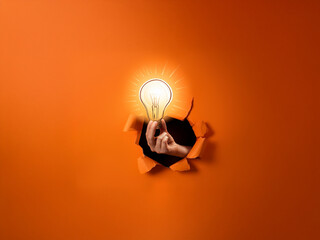 Poster - A hand emerges from a torn orange background, holding a glowing lightbulb; symbolizing a breakthrough idea or innovation.