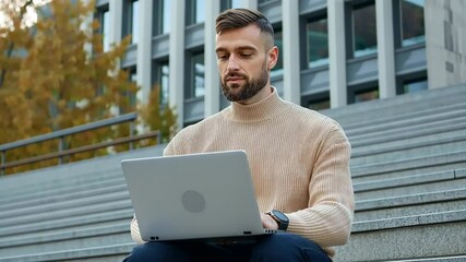 Wall Mural - A man wearing a sweater sits on a staircase with a laptop in front of him