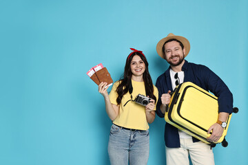 Wall Mural - Tourism. Happy couple with passports, tickets and suitcase on light blue background, space for text