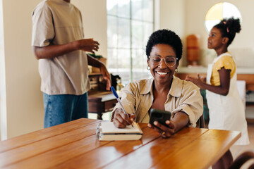 A happy Brazilian family at home: Mom writing in journal while kids smile and use mobile phone