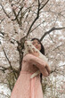 © Milou Dirks - art portrait of young asian woman holding white cat outdoors under sakura cherry blossom tree with flowers in spring