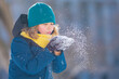 © Volodymyr - Kid blowing snow outdoor. Little boy blowing snow from his hands. Child enjoy walking in the park on snowy day. Kid play with snow. Winter activities for kids in snowy park. Snow kids game.