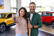 © Graphicroyalty - Visiting car dealership. Beautiful couple is holding a key of their new car, looking at camera and smiling