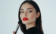 © Azfaribn - Stylish woman with red lips and sleek hair holding a makeup brush against a white background
