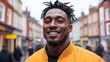 © imagineRbc - A man with dreadlocks wearing a bright orange jacket smiles confidently in a bustling urban street. Colorful buildings and a lively crowd create an engaging atmosphere