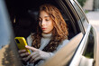 © maxbelchenko - Young woman sitting on backseat of a car and reading text message. Technology, blogging, business concept.