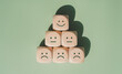 © LAONG - World mental health day concept or feedback rating and positive customer review, wood cube stacking with emotion face icon on pastel green background