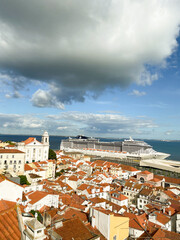 Scenic view of Lisbon's Alfama district with terracotta rooftops, historic church, and a large cruise ship docked at the harbo