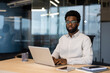 © Liubomir - Portrait of a young serious man inside the office with a laptop. Businessman looking at the camera, working in the evening at the workplace.