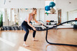 © Iona - Energetic and focused, a woman exercises with battle ropes, embodying strength and endurance in a bright fitness environment.