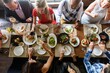 © Rawpixel.com - Diverse friends dining together, sharing food and drinks. Overhead view of people enjoying a meal, socializing, and celebrating around a table with various dishes. Friends having dinner at restaurant.