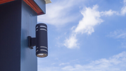 Modern lamp stuck on a pole in front of a house building, bright cloudy sky background. and has space for text