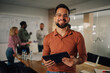 © Zamrznuti tonovi - Smiling businessman holding tablet with coworkers discussing in background