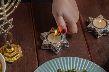 A Jewish woman's hand lights Shabbat candles at the table