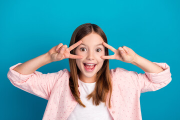 Wall Mural - Smiling young girl making a playful hand sign against a bright blue background