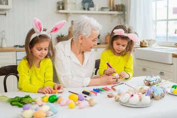 Happy Easter. Two little girls sisters twins grandmother painting eggs enjoying time together. Happy family grandma granddaughters child kids preparing for Easter. Spring Christian festival tradition