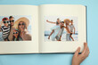 © New Africa - Woman looking at family photos in photo album on light blue background, top view