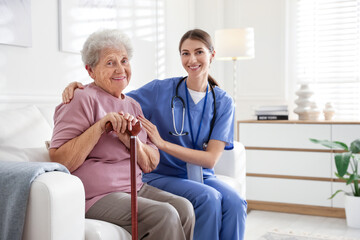 Caregiver supporting senior woman on sofa. Home health care service