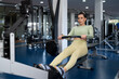 © asier - Female athlete rowing intensely, targeting back muscles and cardiovascular fitness within sleek, contemporary fitness facility