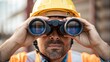 © DigitalSpace - A medium closeup of a crane operators face wearing safety goggles and a hard hat peering through binoculars to observe the cranes movement reflecting the coordination required