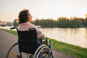 Wall Mural - Sad senior woman sitting in wheelchair walking on road in city outdoor, back view. Old paralyzed lady in chair for people with disability feel depressed. Lonely elderly sick woman sits on wheelchair