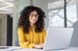 © Liubomir - Joyful and satisfied woman working with laptop inside office, businesswoman typing on keyboard while sitting at desk, office worker smiling wearing shirt and glasses.