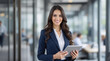 © Nour Studio - Professional portrait of a confident, smiling business woman in a stylish suit, holding a tablet, against a modern office background