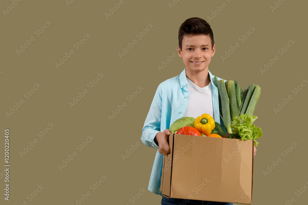 Cute little boy holding cardboard box with different vegetables on green background