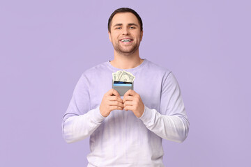 Wall Mural - Young happy man holding wallet with credit card and money on lilac background