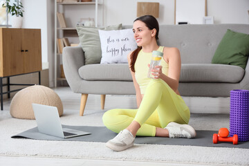 Sticker - Sporty young woman with lemon infused water, laptop and dumbbells sitting on yoga mat at home