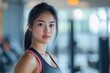 © Stitch - Young Asian woman in athletic wear poses confidently in a brightly lit gym with equipment in the background