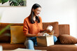 © Home-stock - Satisfied lady received package, unpacking cardboard beauty box with cosmetics and smiling, sitting on couch in living room at home