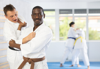 Wall Mural - Two males practicing judo together on sports mats under the guidance of a trainer