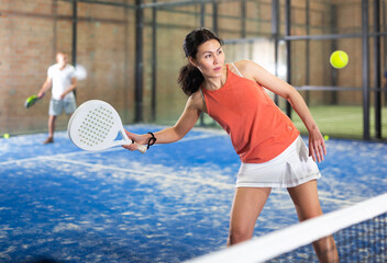 Wall Mural - Young asian woman in orange t-shirt playing padel tennis indoor