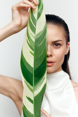 Canvas Print - Young woman holding a large green leaf in front of her face, exuding calmness and confidence, against a minimalist white background.