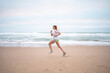 © Andrii - Determined sporty woman running on seashore against sky at beach. Full body of active female athlete is exercising in nature during daytime