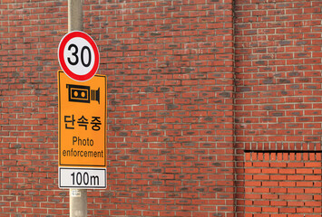 Seongbuk-dong, Seongbuk-gu, Seoul, South Korea - May 4, 2024: Low angle view of road sign with speed ??limit 30km and CCTV Photo enforcement against red bricks of a building