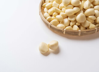 Close up of two peeled raw garlic seeds on white floor with stacked others on bamboo basket, South Korea